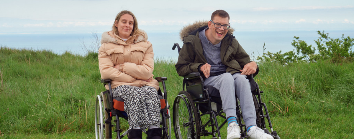 two people on wheelchairs at the top of a cliff facing the camera and smiling