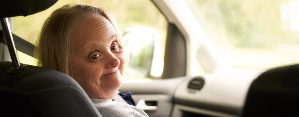 Down syndrome woman in passenger seat of a car turning and smiling at the camera 
