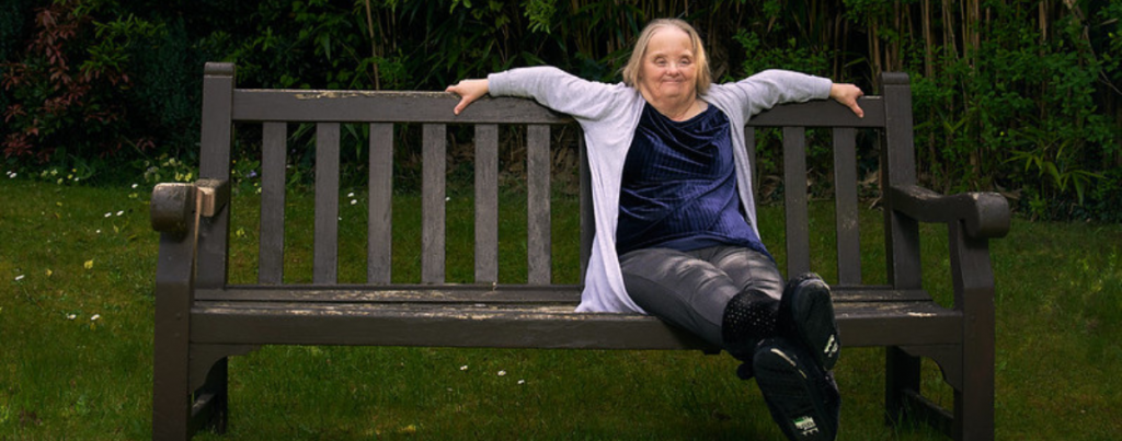A woman with down syndrome sat happily and independently on a bench