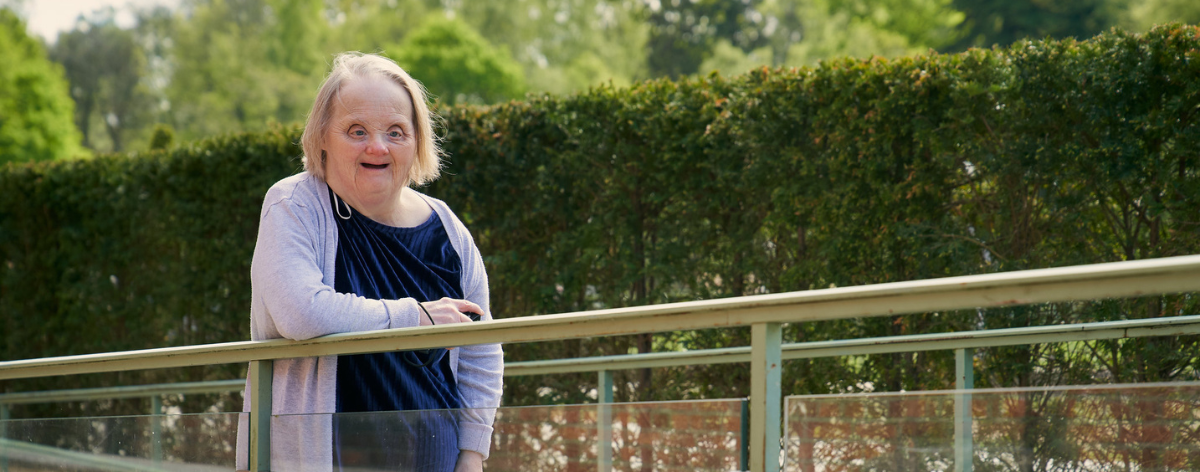 Down syndrome woman posing for photo by leaning over a bannister of a walkway